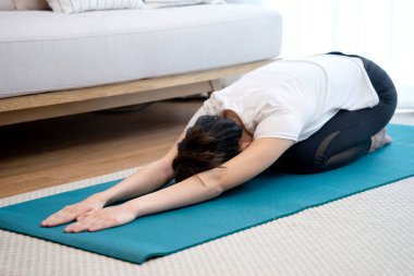 Yoga egzersizi yapan genç bir kadın evdeki kanepenin yanındaki minder üzerinde poz veriyor.