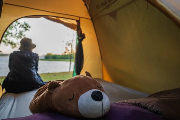 Seçici olarak çadırdaki kahverengi oyuncak ayıya, Asyalı kadın tatilde tatil pikniğine, göl kenarında dinlenmeye odaklanmış..