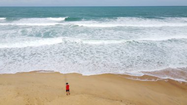 Sahilde beyaz dalgalı erkek turist, kumlu sahilde mavi okyanus dalgası.