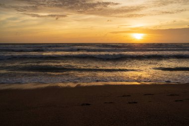 Renkli okyanus plajı günbatımı, turuncu ve altın gün batımı gökyüzü.