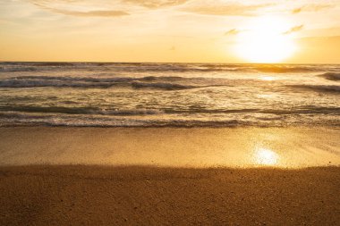 Renkli Turuncu ve altın rengi günbatımı gökyüzü, suda güneşin yansıması ve kumsalda kum..