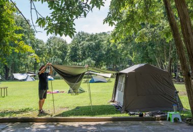 Açık hava turistleri çim ya da yeşil çimlerin altına kamp çadırı kuruyor tatilde ağaçların altına tatil pikniği, tatilde dinlenme, kamp sezonu..