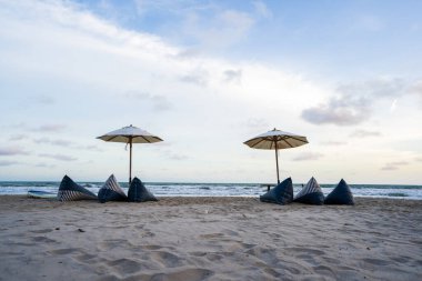 Koltukları ve deniz kenarında şemsiyeleri olan kumsal, kum ve mavi gökyüzü..