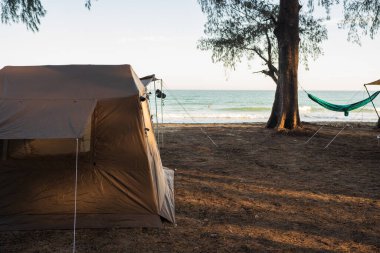 Kumsaldaki ağaçların altındaki çadırlarda kamp yapan turistler..