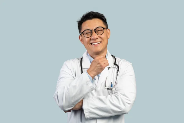 幸せな中高年の中国の男性医師の白いコートで 眼鏡をカメラでは 青の背景に孤立して見てください Covid 19パンデミック — ストック写真