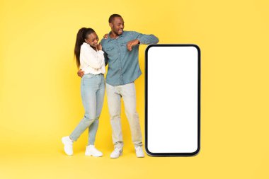 Sarı arka planda Stüdyo 'da boş ekranda duran ve poz veren Afrikalı Amerikalı çift. Gadget ve Teknoloji Konsepti. Model