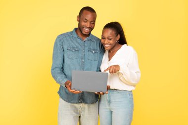 Mutlu siyah çift birlikte dizüstü bilgisayar kullanarak interneti tarıyor ve sarı stüdyonun arka planında çalışıyor. IT Teknoloji ve E-Öğrenme Konsepti