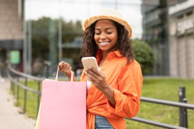 Bin yıllık Afro-Amerikan bayanı, gündelik giyinmiş, şapkalı, çantalı, akıllı telefonuyla şehir caddesinde yazı yazan özgür bir yer. Çevrimiçi alışveriş, nakit para, sosyal ağ, blog ve yaşam tarzı uygulaması