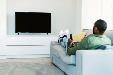 Siyah adam boş ekranlı televizyon izliyor, elinde uzaktan kumanda var ve düz ekran plazmada kanal değiştiriyor, evdeki kanepede oturuyor, hafta sonunu içeride geçiriyor. Model