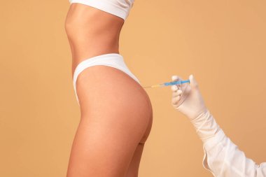 Non-sugical butt lifting sculptra concept. Side view of young woman getting hip injection at buttocks area, isolated on beige studio background, cropped