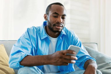 Yakışıklı Afro-Amerikalı adam kanepede oturup sohbet ediyor. Akıllı telefondan, ev içi ve fotokopi alanından flört uygulaması kullanıyor. Milenyum konsepti için Gadget bağımlılığı