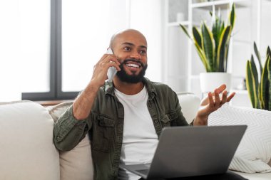 Kanepede dizüstü bilgisayarla otururken cep telefonuyla konuşan pozitif Latin işadamı, kopyalama alanı. Telefonla konuşan bir adam iş görüşmesi yapıyor. İletişim önlemi