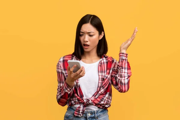 没有无线保真有智能手机的令人失望的中国女士有着互联网或网络连接问题 站在黄色工作室的背景之上 — 图库照片
