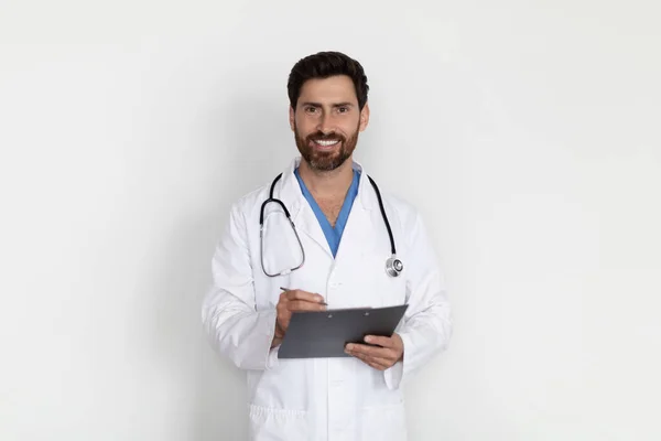 医疗服务 照片中穿着制服 手持剪贴板 看着相机的英俊男性医生的画像 他是位体格健壮 背景洁白 复印空间强的医生 — 图库照片