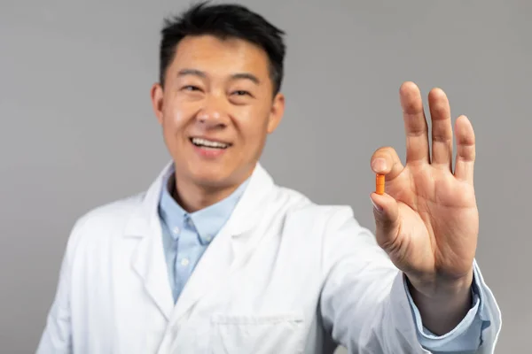 Uśmiechnięty Koreański Lekarz Średnim Wieku Białym Płaszczu Pokazuje Kapsułkę Lekarską — Zdjęcie stockowe