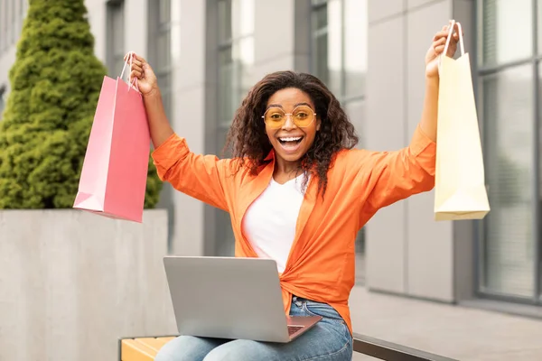 若いアフリカ系アメリカ人女性のカジュアルとガラスのラップトップで多くのパッケージを拾うとショックを受け 街の通りで注文を楽しんでいます 素晴らしいオンラインショッピング キャッシュバック 巨大な販売 デジタル広告やオファー — ストック写真