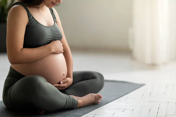 お待ちしております 若い妊娠中の女性はヨガマットに座って 腹を受け入れます 自宅で瞑想を練習しながら 認識できない期待外れの女性はおなかに触れます クロップ — ストック写真