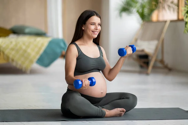 国内培训 快乐的孕妇在家用哑铃做运动 年轻孕妇穿着运动服在客厅的健身垫上锻炼 享受健康的生活 — 图库照片