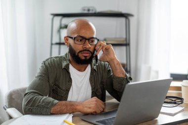 Laptop 'ta çalışırken cep telefonundan arayan Latin erkek serbest yazar, evde telefon görüşmesi yapıyor. İş iletişimi ve girişimcilik kavramı
