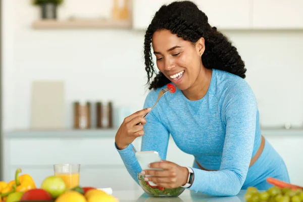 减肥应用程序 快乐的黑人女士一边吃蔬菜沙拉一边用智能手机 在厨房里享受午餐 复制空间 膳食营养 瘦身申请 — 图库照片