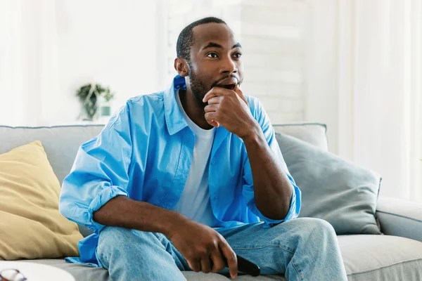 家でテレビを見ている 感情的なアフリカ系アメリカ人の男は リモートコントローラ フリースペースでチャンネルを切り替える 休息を持っている 黒人男性は週末を楽しんで興味深いプログラムを見て — ストック写真
