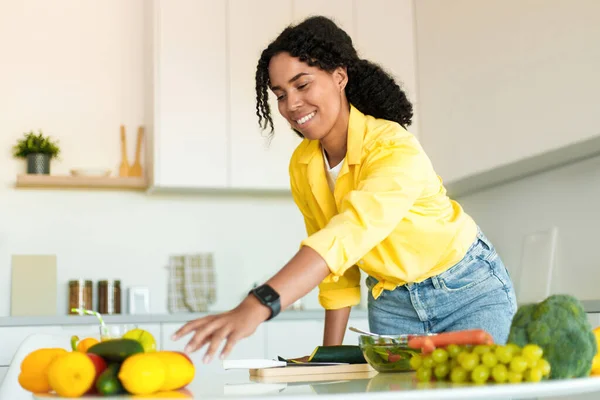 Healthy food to boost your immune system. Young african american woman cooking fresh organic salad at home in modern kitchen, reaching for vegetables, free space