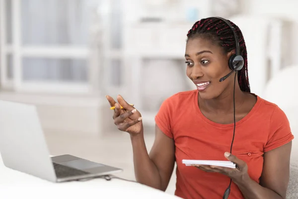 Online Tutoring. Black Young Woman In Headset Having Video Conference On Laptop, Smiling African American Female Talking And Gesturing At Web Camera During Virtual Lesson, Sitting At Desk At Home