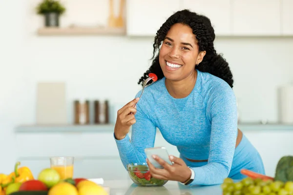 Happy Black Lady Sportswear Eating Salad Home Kitchen Leaning Table — Stock Photo, Image