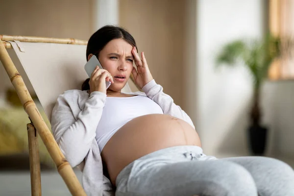 Bezorgde Zwangere Vrouw Praten Mobiele Telefoon Tijdens Het Zitten Stoel — Stockfoto
