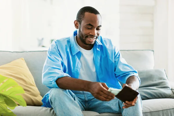 Hombre Negro Positivo Casual Poniendo Dinero Cartera Sonriendo Sentado Sofá —  Fotos de Stock