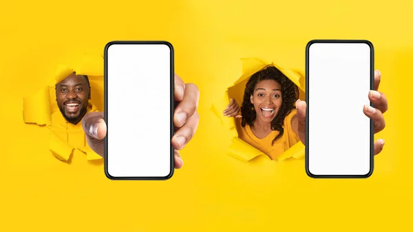 背の高い黄色い紙の背景に穴を通ってカメラに腕を伸ばすブランクスクリーンで携帯電話を示す黒人男性と女性 モバイルアプリケーション広告 パノラマ モックアップ — ストック写真