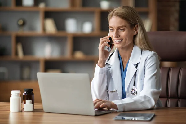 Χαμογελώντας Γιατρός Γυναίκα Μιλώντας Στο Κινητό Τηλέφωνο Και Χρησιμοποιώντας Φορητό — Φωτογραφία Αρχείου
