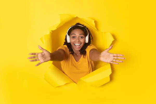 カメラに腕を伸ばすヘッドフォンを装着した喜びに満ちた黒人女性が黄色い背景で音楽を聴く 素晴らしいプレイリストと音楽ガジェットのコンセプト — ストック写真
