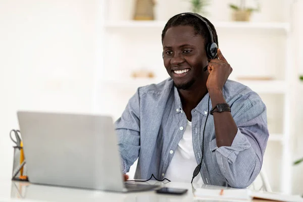 Remote Job. Happy Black Male Wearing Headset Using Laptop For Online Work, Smiling Young African American Man In Headphones Sitting At Desk In Home Office And Working On Computer, Copy Space