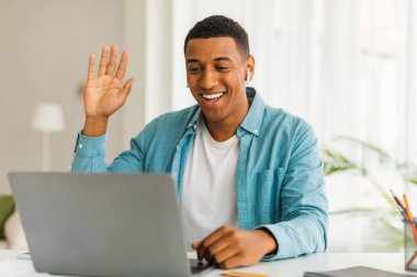 Bin yıllık Afro-Amerikan erkek menajeri dizüstü bilgisayarla el sallıyor, video görüşmesi yapıyor, oturma odasının içinde online ders veriyor. Özel ders, eğitim, evde buluşma, sosyal mesafe, covid-19 salgını