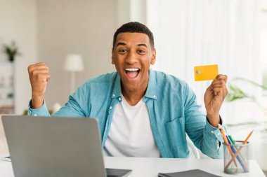 Bin yıllık Afro-Amerikan erkeğinin laptoplu ve kredi kartlı ağzı açık şekilde zafere, oda içinde başarıya sevinmesine sevindim. Harika bir anlaşma, online alışveriş, büyük indirimli para ve duygular.