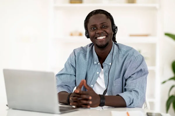 Remote Career. Happy Young Black Man In Headset Posing At Desk With Laptop And Smiling At Camera, Cheerful Millennial African American Male Enjoying Online Work Opportunities, Copy Space