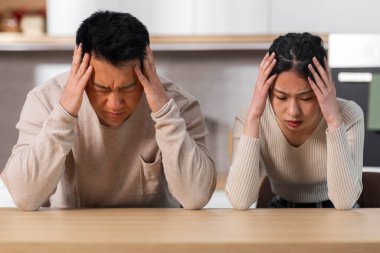 Evdeki mutfak masasında oturan üzgün Asyalı eşler, başlarını okşayıp, aşağı bakıyorlar, zavallı aç Asyalı aile kocası ve karısı açlıktan ölüyor, 2022 krizi sırasında yiyecek hiçbir şeyleri yok, yakın plan portreleri.