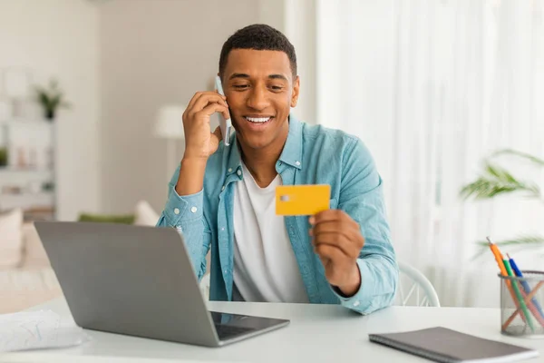 Uśmiechnięty Afrykańczyk Dzwoni Przez Telefon Używa Karty Kredytowej Laptopa Wnętrzu — Zdjęcie stockowe