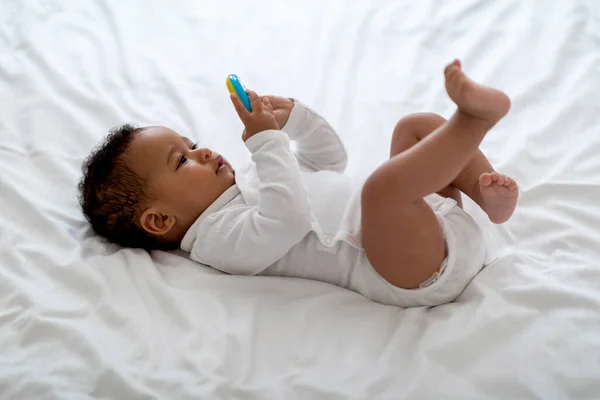 Siyah Bebeğin Yatakta Yatarken Çıngıraklı Bebeklerle Oynarken Çekilmiş Yan Görüntüsü — Stok fotoğraf
