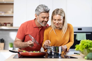 Modern mutfakta orta yaşlı güzel bir kadın ve erkek birlikte yemek pişiriyor, pofuduk bir çift evde sağlıklı bir akşam yemeği hazırlıyor. Sağlıklı yaşam tarzı, diyet, beslenme konsepti