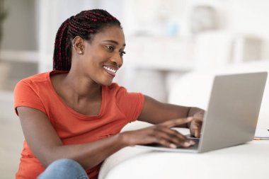 Gülümseyen Afrikalı Amerikalı kadın dizüstü bilgisayarında internete bakıyor, masada oturan, bilgisayarında yazan, arkadaşlarıyla internetten alışveriş yapan ya da mesajlaşan mutlu siyah kadın,