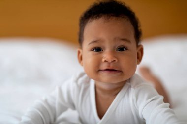 Yakından bakınca, gülümseyen küçük siyah bebek yatakta dinleniyor, sevimli Afrikalı Amerikalı bebek ya da kız göbeğinde uzanıyor ve evde dinlenirken kameraya bakıyor.