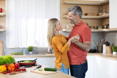 Yetişkin eşlerin mutfakta birlikte yemek pişirirken dans etmesi, orta yaşlı yakışıklı adamın güzel sarışın karısıyla evde romantik bir akşam geçirmesi, fotokopi çekmesi. İlişki, evlilik, aile.
