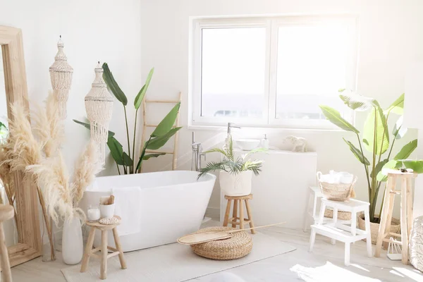 Interior Shot Of Light Stylish Bathroom In Boho Style With Rustic Decorations, Big Spacious Bathing Room With White Bath Tube Inside, Natural Green Plants And Big Window, Free Space