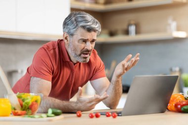 Kızgın, gri saçlı, orta yaşlı adam bilgisayar ekranına bakıyor, evde tek başına yemek pişirirken el kol hareketi yapıyor, kocası yemek hazırlarken zorlanıyor, internette yemek tarifi okuyor, uzayı kopyalıyor.