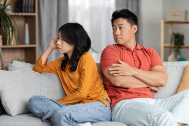Boşanma, ilişki krizi, evlilik ve çelişki konsepti. Evdeki kanepede oturan üzgün Asyalı çift, ev elbiseli mutsuz Çinli erkek ve kadın kavga ediyorlar, birbirleriyle konuşmuyorlar.