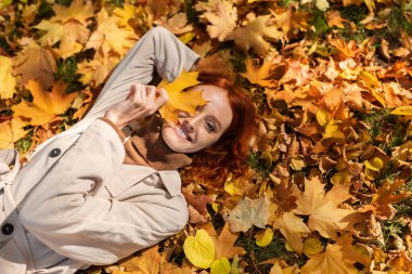 Gülümseyen Avrupalı kızıl saçlı kadın yerde yatıyor, sonbaharda şehirde gözüne sarı yaprak sürüyor. Dinlen ve rahatla, kadın boş zamanın ve hafta sonunun tadını çıkar, yalnız eğlenmene bak.