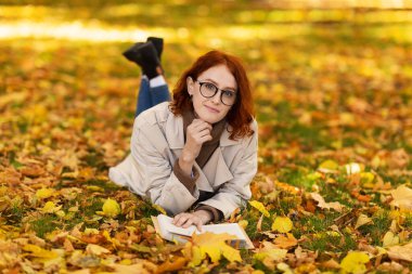 Sonbaharda kentte parkta kitap okuyan, gözlüklü, sarı yapraklı, kızıl saçlı, ciddi bir Avrupalı genç bayan. Hobi, dinlenme ve boş vakitte dinlenme, kadın şehir dışında hafta sonunun tadını çıkar.