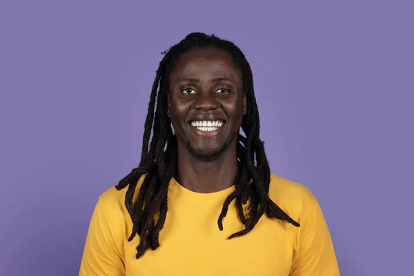 黄色のTシャツを着て 紫のスタジオの背景に笑みを浮かべて長いブライドを持つ陽気なアフリカ系アメリカ人の千年男のクローズアップ肖像画 黒人は概念に直面する — ストック写真